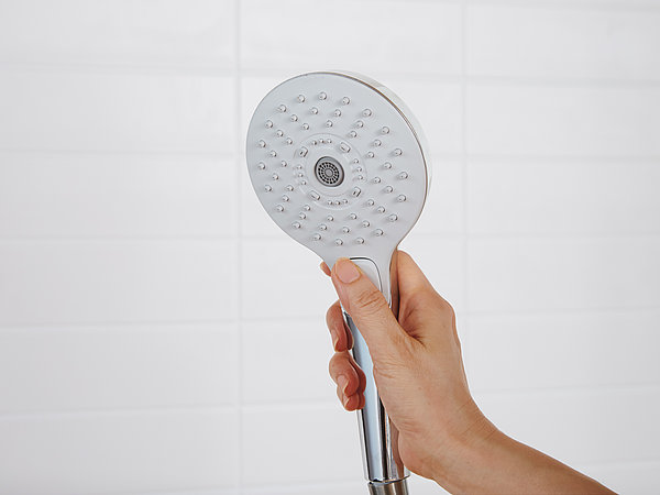One hand holds up a TOTO shower head. The shower head is switched off.