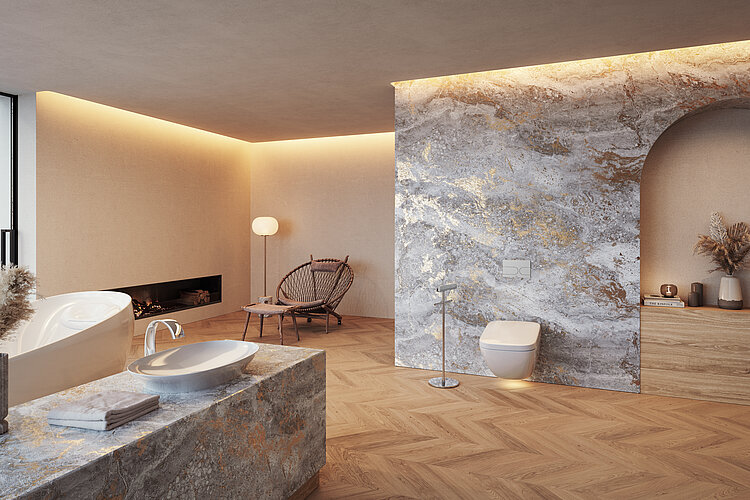 Das Foto zeigt ein modernes Badezimmer mit einer freistehenden Badewanne, einer bodengleichen Dusche hinter einer marmorierten Wand mit einer Bogenöffnung, einer Waschtischinsel und einer Wandtoilette. Der Raum ist warm beleuchtet, mit indirektem Licht an der Decke und einer Stehlampe, und enthält eine Sitzecke mit einem Designerstuhl, was eine wohnliche Atmosphäre schafft.