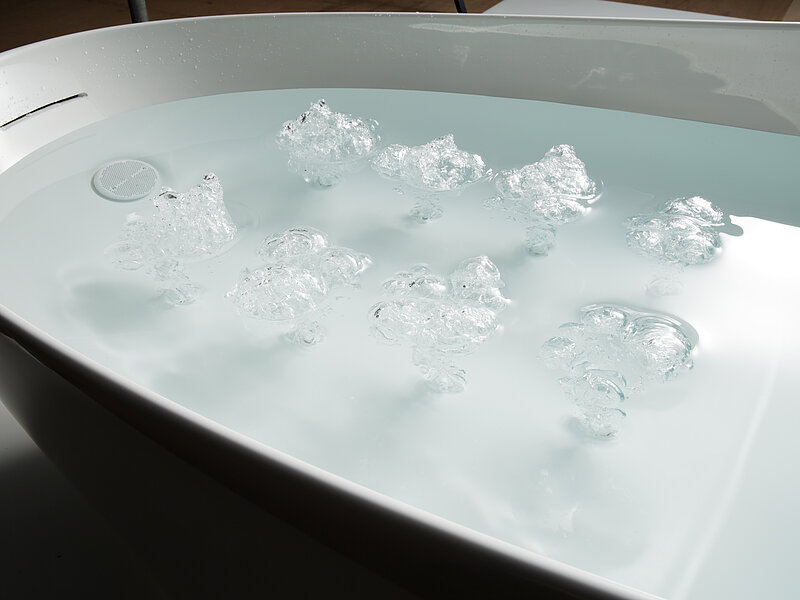 Eight clusters of bubbles created by swirls break through the surface of the water in the bathtub.