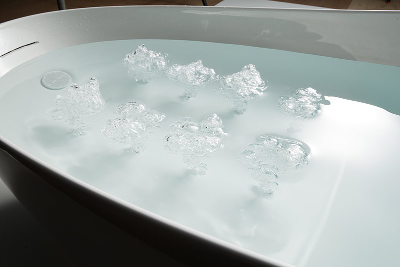 Eight clusters of bubbles created by swirls break through the surface of the water in the bathtub.