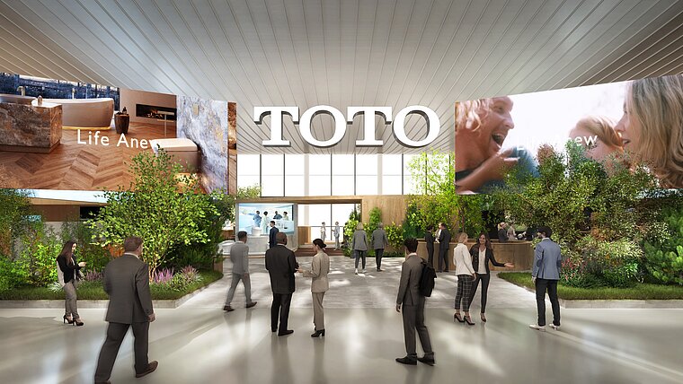 The image shows a computer-generated representation of TOTO's entrance area at the ISH trade fair, characterized by a large brand name on the wall and several screens displaying promotional content. The scene is animated with numerous visitors moving through an open hall surrounded by plants and well-lit, creating an inviting and interactive atmosphere.
