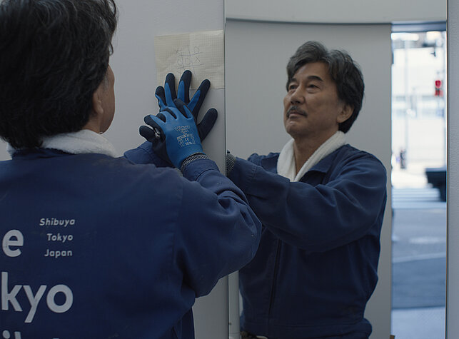 Hirayama steht vor einem Spiegel in einer öffentlichen Toilette. 