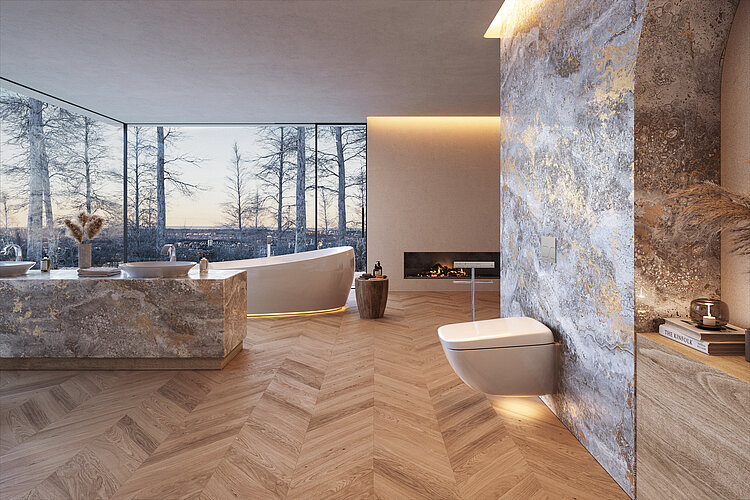 Das Bild zeigt ein luxuriöses Badezimmer bei Dämmerung mit großen Panoramafenstern, die einen Blick auf kahle Bäume und den Abendhimmel bieten. Im Vordergrund ist eine wandhängende Toilette zu sehen, daneben ein Waschtisch aus Naturstein und eine freistehende Badewanne; ein Kaminfeuer trägt zur behaglichen Atmosphäre bei.