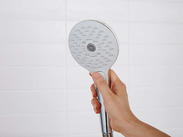 Une main tient une pomme de douche TOTO en l'air. La pomme de douche est éteinte.