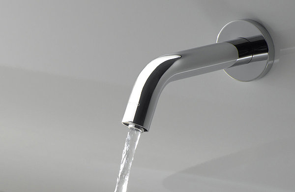 Un robinet est installé sur un mur au-dessus d'un lavabo. Le robinet est allumé et un jet d'eau en sort. 