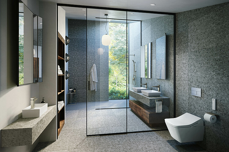 Das Bild zeigt ein geräumiges, modernes Badezimmer mit einer großen, begehbaren Dusche aus Glas, grauen Wandfliesen und einer Aussicht auf Bäume im Hintergrund. Es gibt eine schwebende Eitelkeit mit einem Doppelwaschbecken, Holzakzenten und einem beleuchteten Spiegel darüber.
