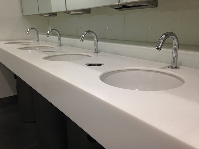 Four undercounter washbasins with touch-free faucets in a public bathroom