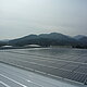 The picture shows a collection of solar panels on the roof of a building with a mountain landscape in the background.
