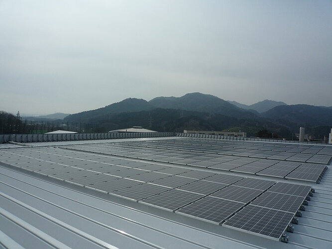 The picture shows a collection of solar panels on the roof of a building with a mountain landscape in the background.